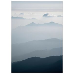 Layered mountain ranges in atmospheric perspective, with forested foreground darkening to misty peaks and clouds in the distance.